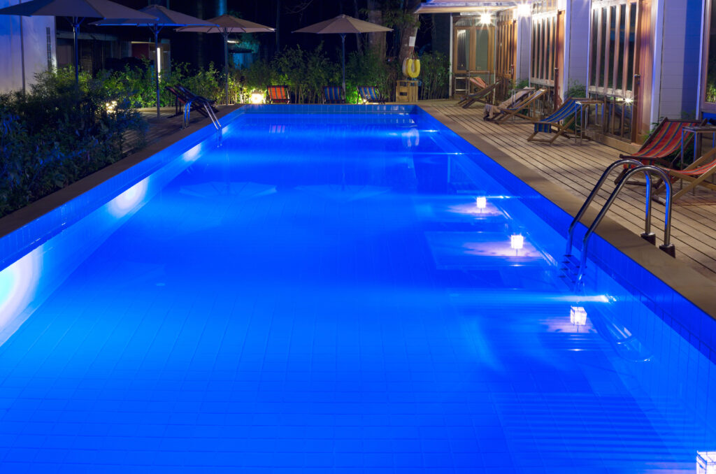 A deep blue illuminated rectangle pool at night, designed by pool builders in Bakersfield CA.